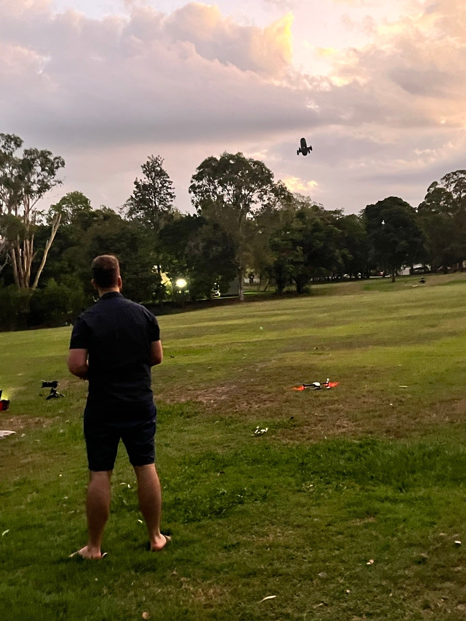 A pilot flying a drone over an open field at dusk